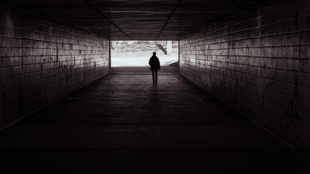 Self-defense tips illustrated by a person walking alone through a dark tunnel, emphasizing situational awareness.